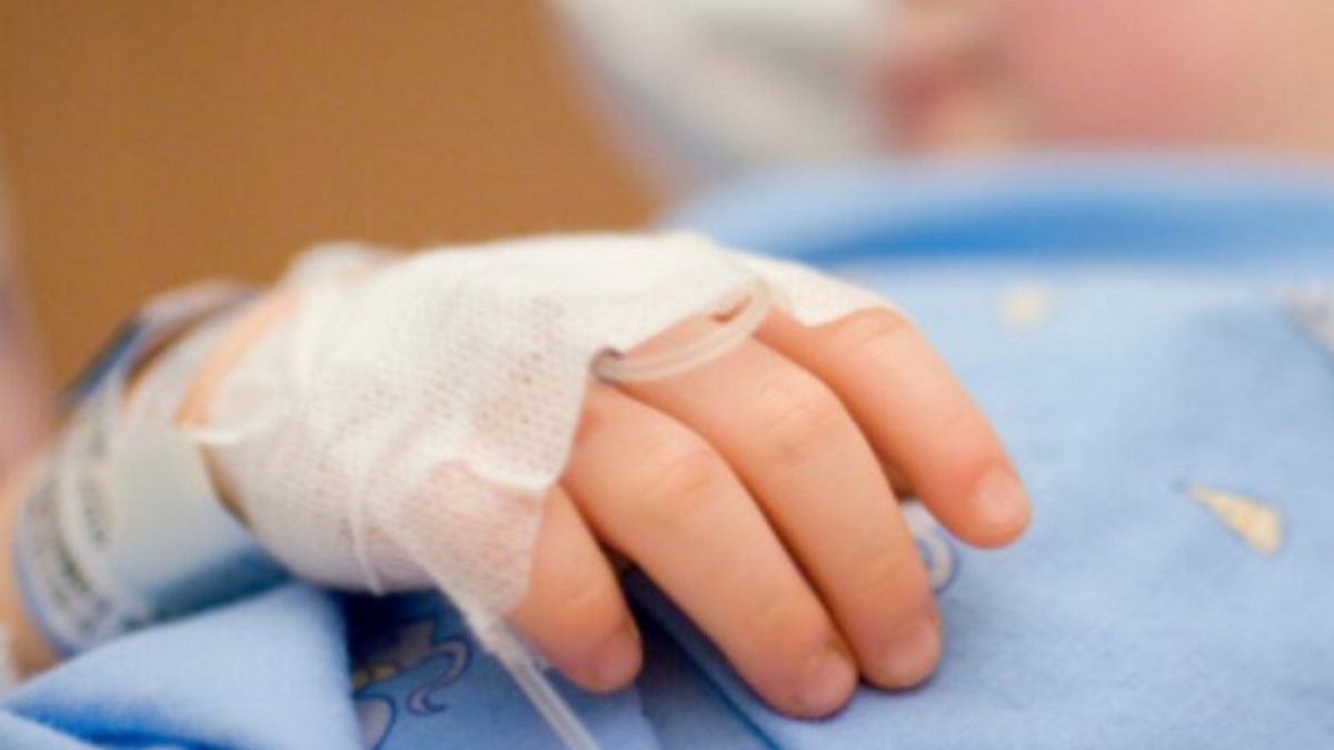 "Close up of the hand of a little girl, lying in a hospital bed. Hand is tied down, with tube for an infusion. Focus on the hand."